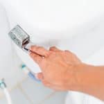 A person’s hand is pressing down the chrome flush handle on a white toilet in a bathroom. The photo, taken from above, also hints at the surrounding plumbing often inspected during Boiler Service NYC checks. A person’s hand is pressing down the chrome flush handle on a white toilet in a bathroom. The photo, taken from above, also hints at the surrounding plumbing often inspected during Boiler Service NYC checks.