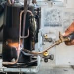 A person uses a blowtorch to weld copper pipes on the compressor unit of an air conditioning system during a repair or maintenance process, similar to techniques used in professional Boiler Service NYC. A person uses a blowtorch to weld copper pipes on the compressor unit of an air conditioning system during a repair or maintenance process, similar to techniques used in professional Boiler Service NYC.